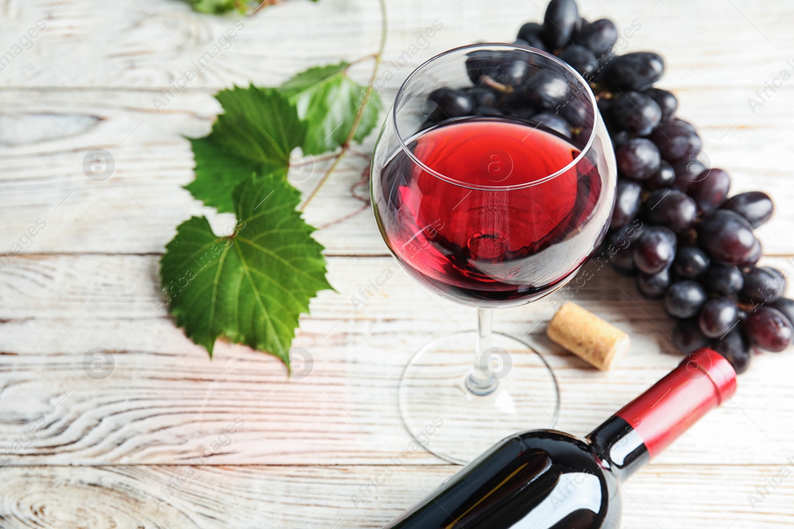 Photo of Glass and bottle of red wine with fresh ripe juicy grapes on table