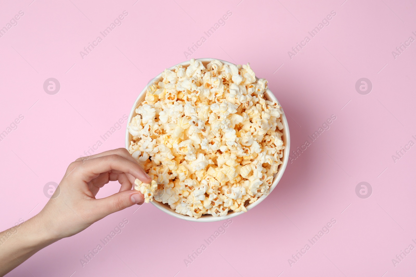 Photo of Woman eating tasty popcorn from paper bucket on color background, top view