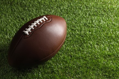 Leather American football ball on green grass. Space for text