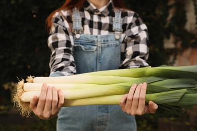 Photo of Woman holding fresh raw leeks outdoors, closeup