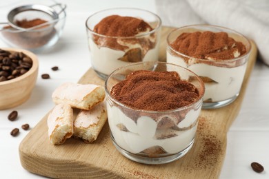 Delicious tiramisu in glasses, cookies and coffee beans on white table, closeup