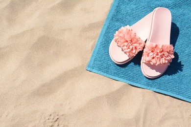 Towel and stylish flip flops on sand, above view with space for text. Beach accessories