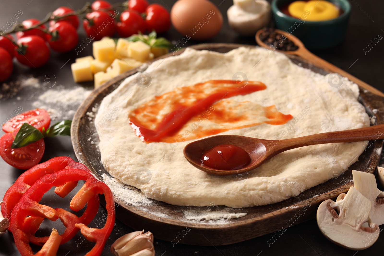 Photo of Pizza dough with tomato sauce and products on dark table, closeup