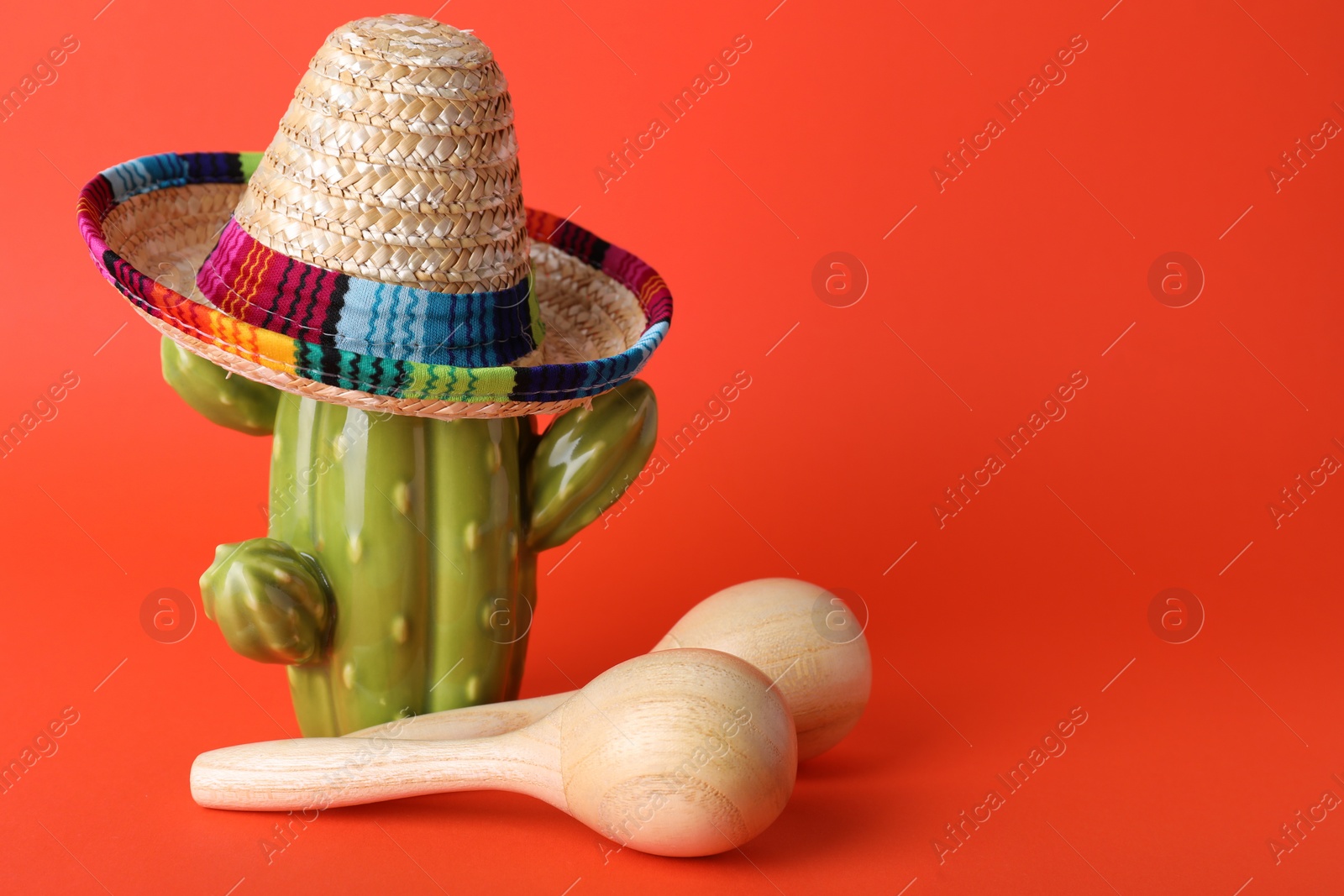 Photo of Wooden maracas and toy cactus with sombrero hat on red background, space for text. Musical instrument
