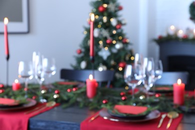 Elegant Christmas table setting with dishware and burning candles in festively decorated room, blurred view
