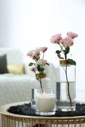 Photo of Burning candle and vases with beautiful roses on table indoors. Interior elements