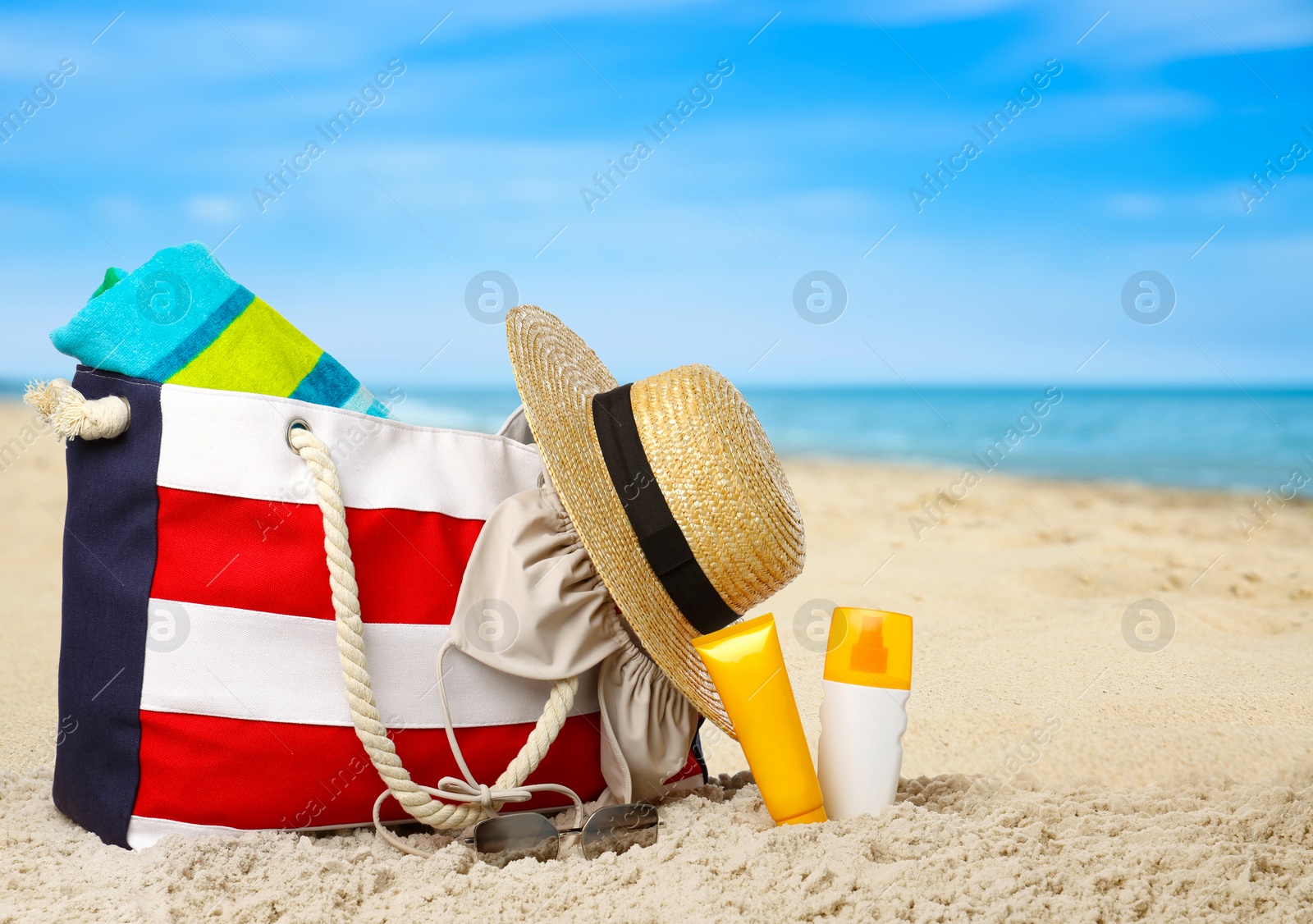 Image of Stylish bag with different accessories on sandy beach near ocean