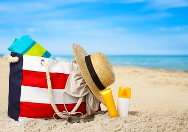 Image of Stylish bag with different accessories on sandy beach near ocean