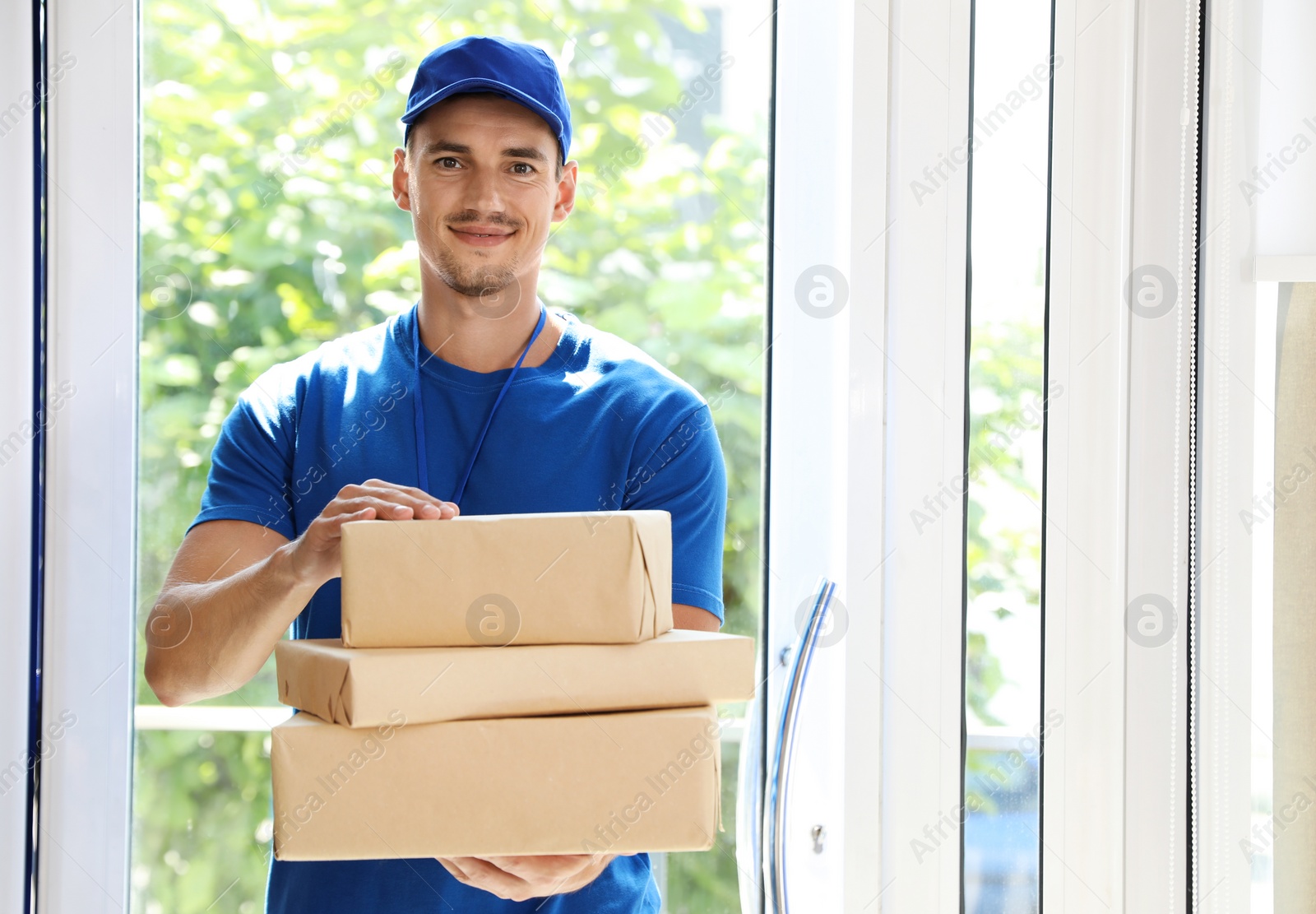 Photo of Happy young courier with pile of parcels in doorway. Space for text