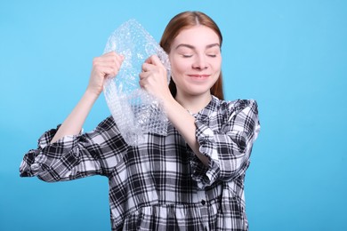 Woman popping bubble wrap on turquoise background. Stress relief