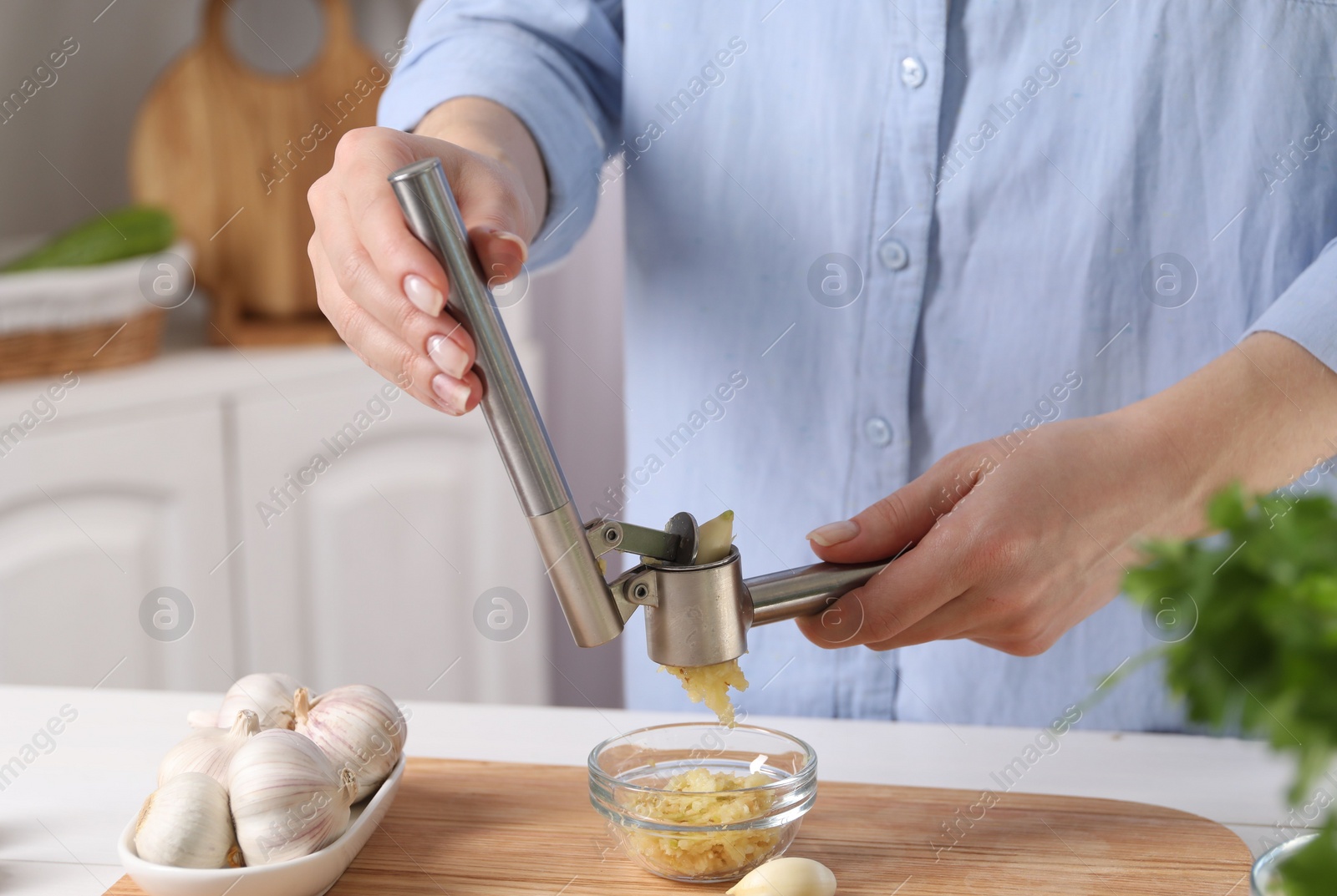 Photo of Woman squeezing garlic with press at white table in kitchen, closeup