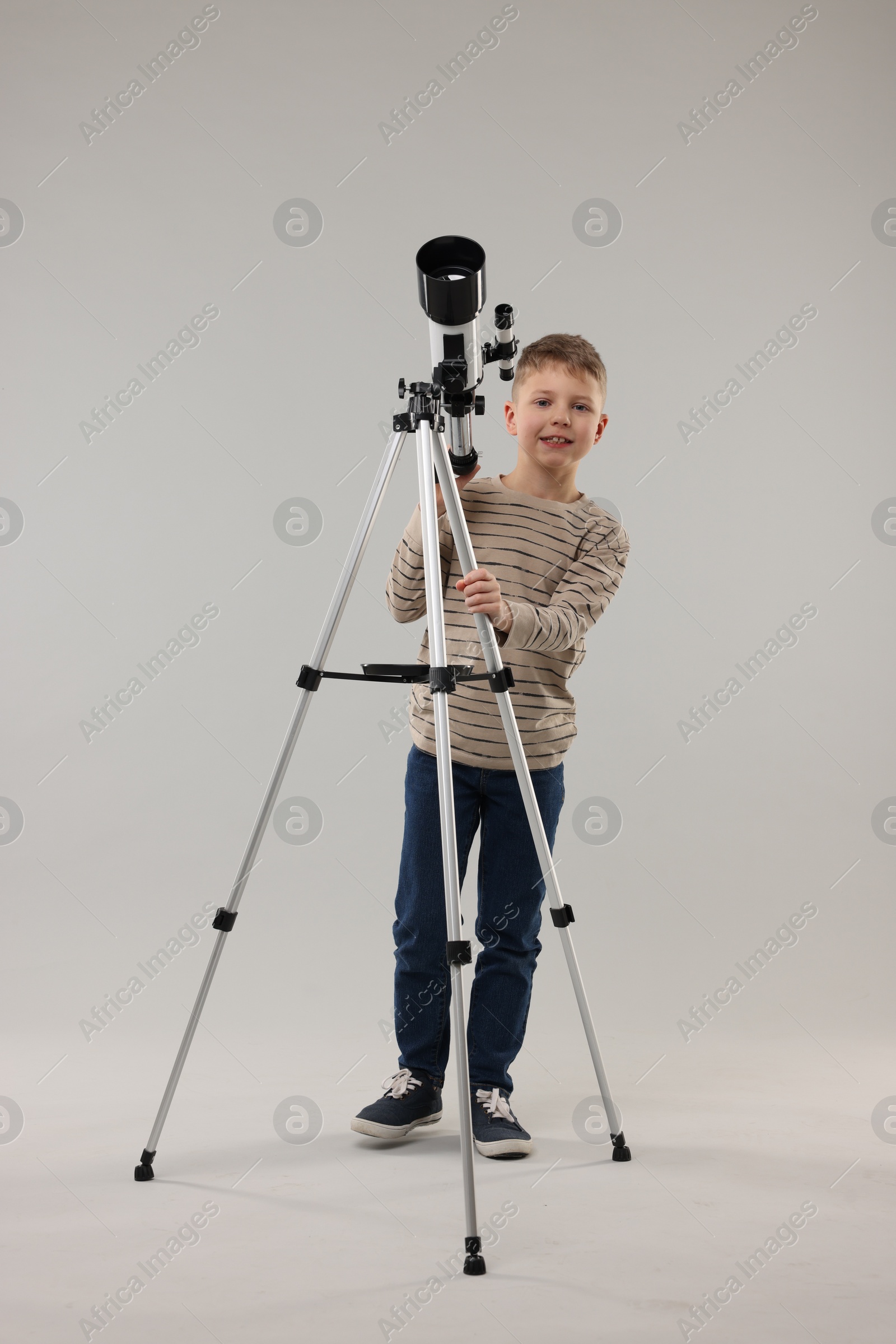 Photo of Cute little boy with telescope on light grey background