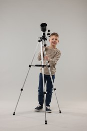 Cute little boy with telescope on light grey background