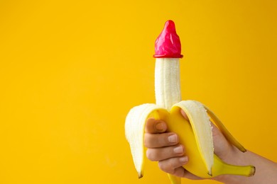 Photo of Woman holding banana in condom on orange background, closeup and space for text. Safe sex concept