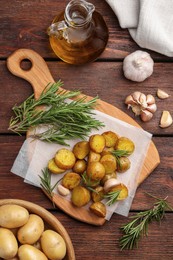 Delicious baked potatoes with rosemary and garlic on wooden table, flat lay