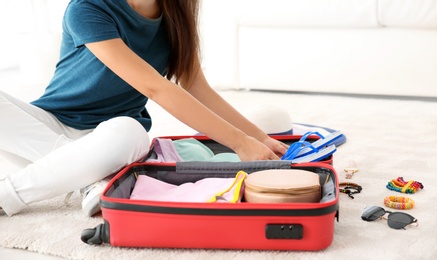 Young woman packing suitcase for summer journey at home