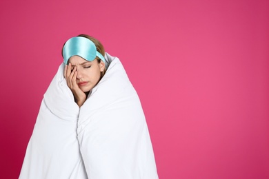 Young woman in sleeping mask wrapped with soft blanket on pink background. Space for text