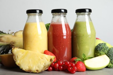 Photo of Bottles of delicious juices and fresh fruits on grey table