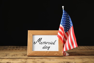 Frame with phrase Memorial Day and American flag on wooden table against black background