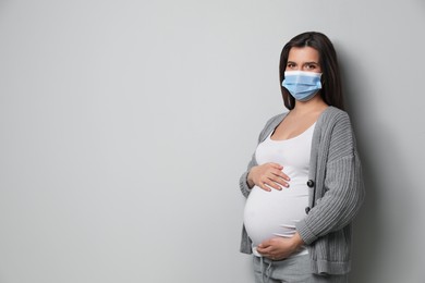 Young pregnant woman in medical mask on grey background, space for text