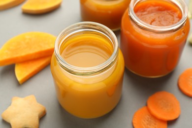 Jars with healthy baby food, pumpkin, carrot and cookie on grey background, closeup