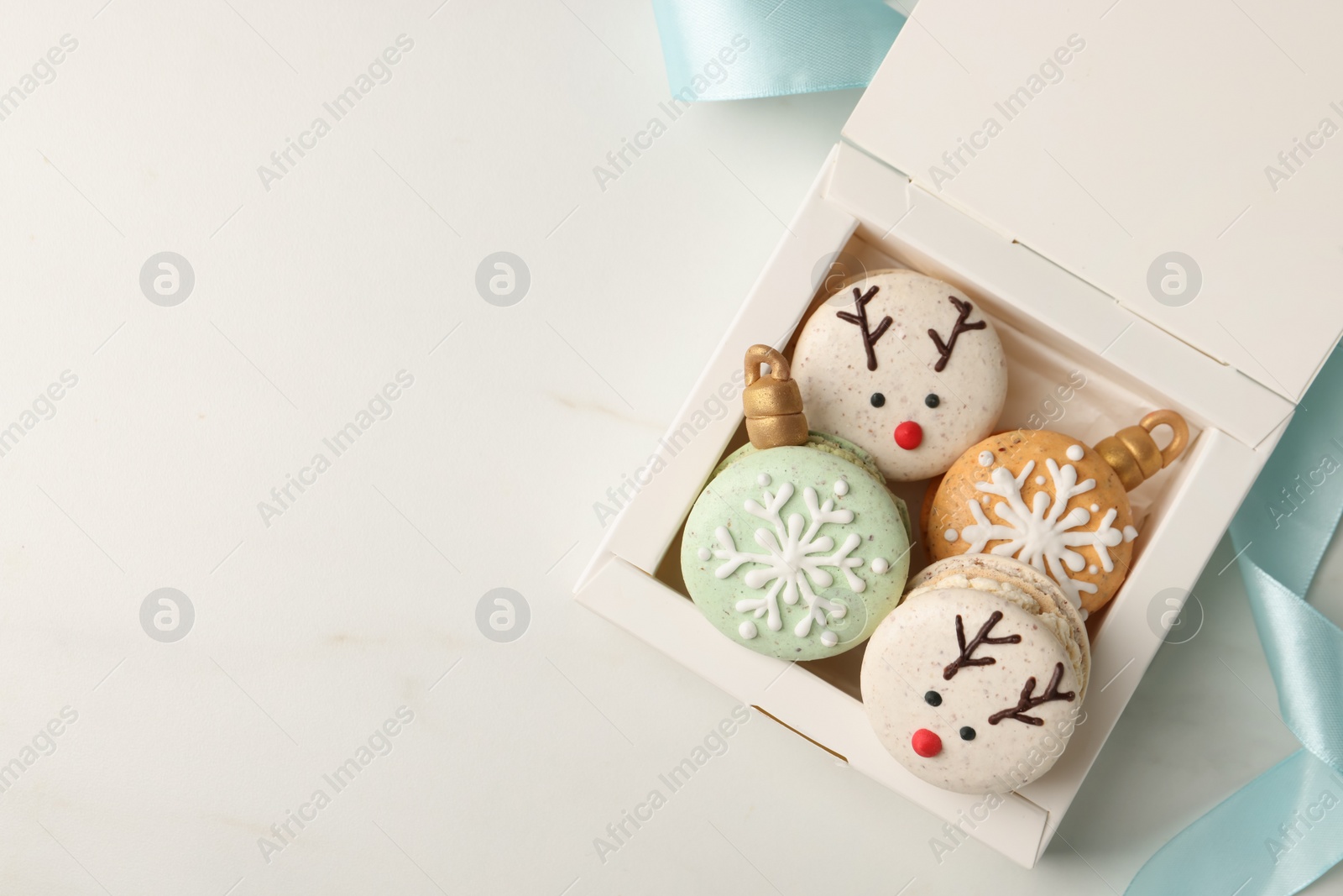 Photo of Beautifully decorated Christmas macarons in box and ribbon on white table, flat lay. Space for text