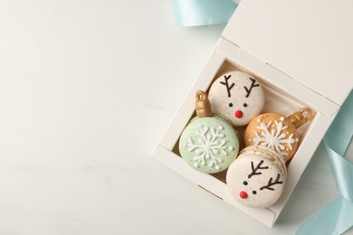 Photo of Beautifully decorated Christmas macarons in box and ribbon on white table, flat lay. Space for text