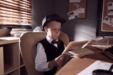 Photo of Cute little detective reading newspaper in office