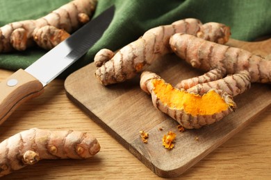 Many raw turmeric roots and knife on wooden table