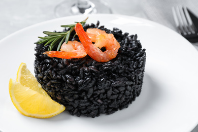 Delicious black risotto with shrimps and lemon in plate, closeup