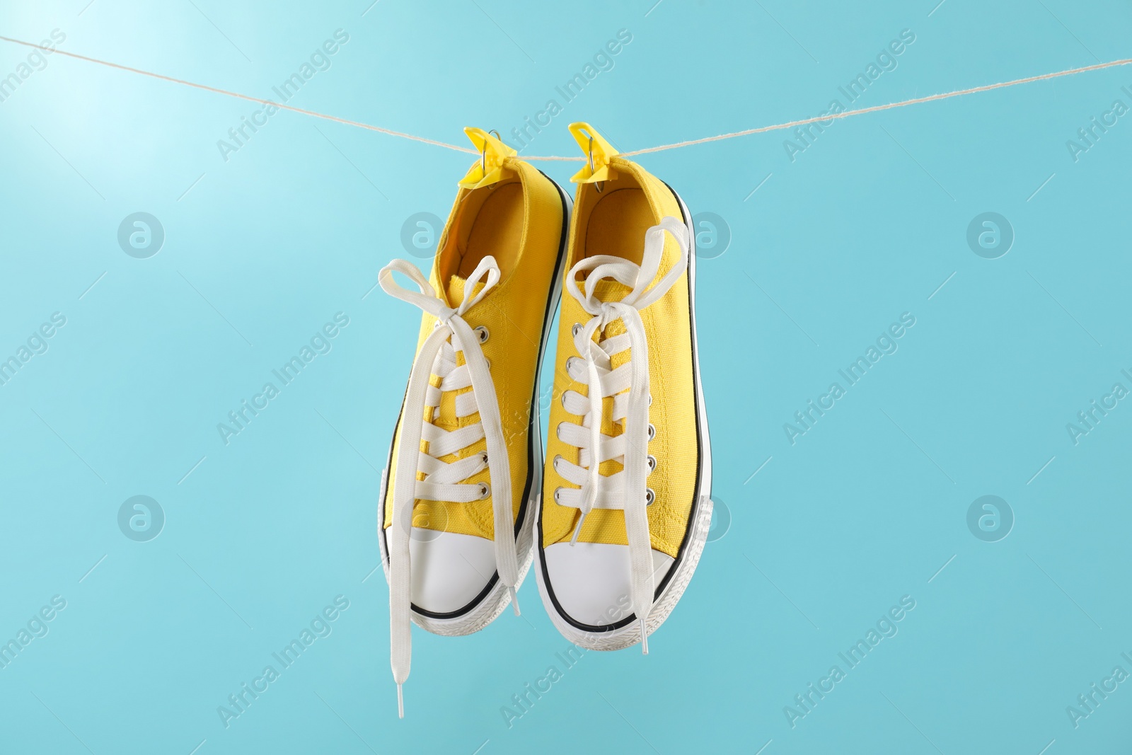 Photo of Stylish sneakers drying on washing line against light blue background