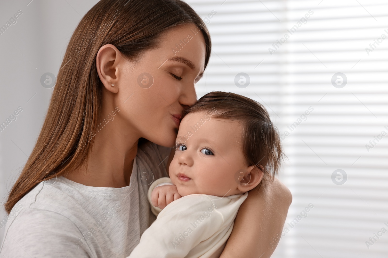 Photo of Happy mother kissing her little baby indoors