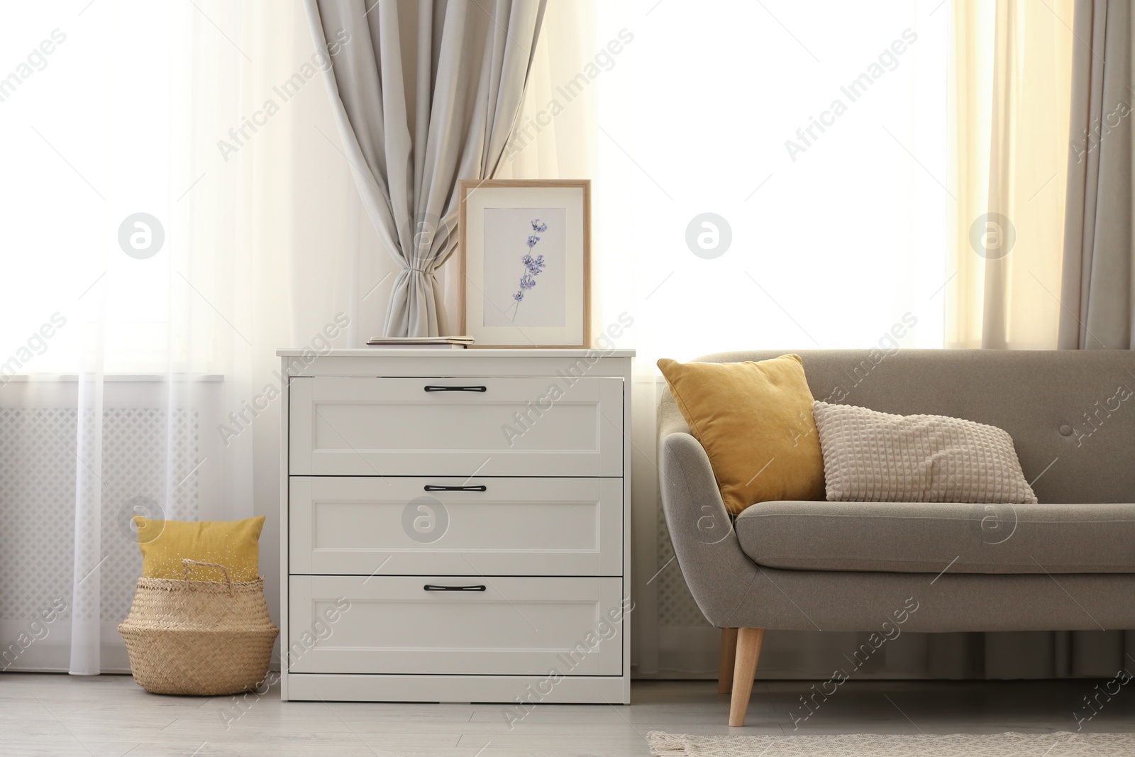 Photo of Sofa and chest of drawers near window with stylish curtains in living room. Interior design