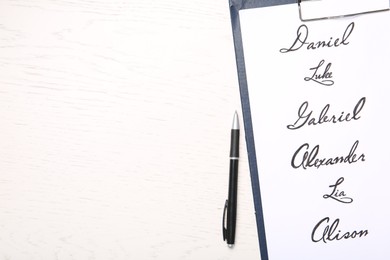 Photo of Clipboard with written different baby names and pen on white wooden table, flat lay. Space for text