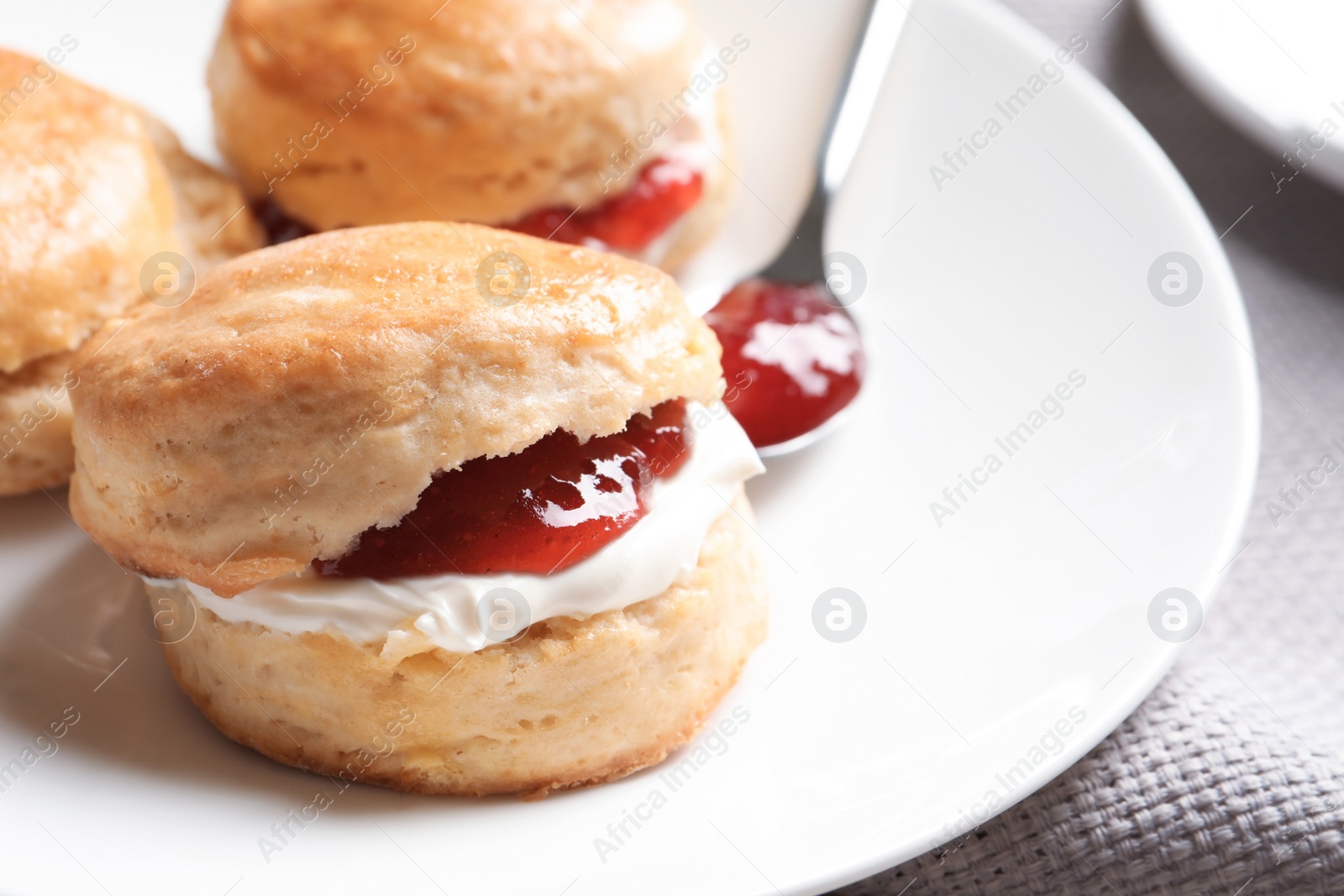 Photo of Tasty scones with clotted cream and jam on plate, closeup