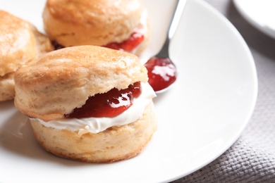 Photo of Tasty scones with clotted cream and jam on plate, closeup