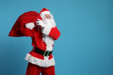 Photo of Santa Claus with bag of Christmas gifts on light blue background, space for text