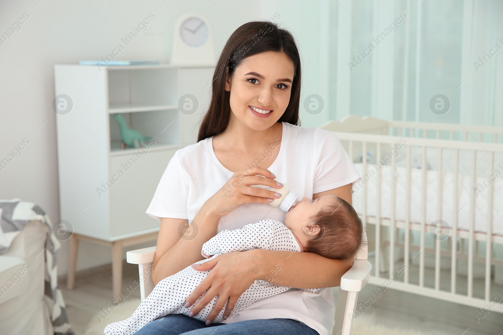 Photo of Woman feeding her baby from bottle in nursery at home