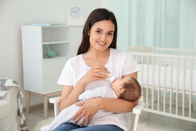 Photo of Woman feeding her baby from bottle in nursery at home