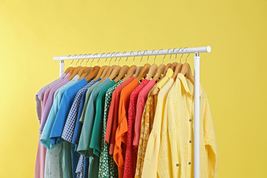 Photo of Bright clothes hanging on rack against yellow background. Rainbow colors