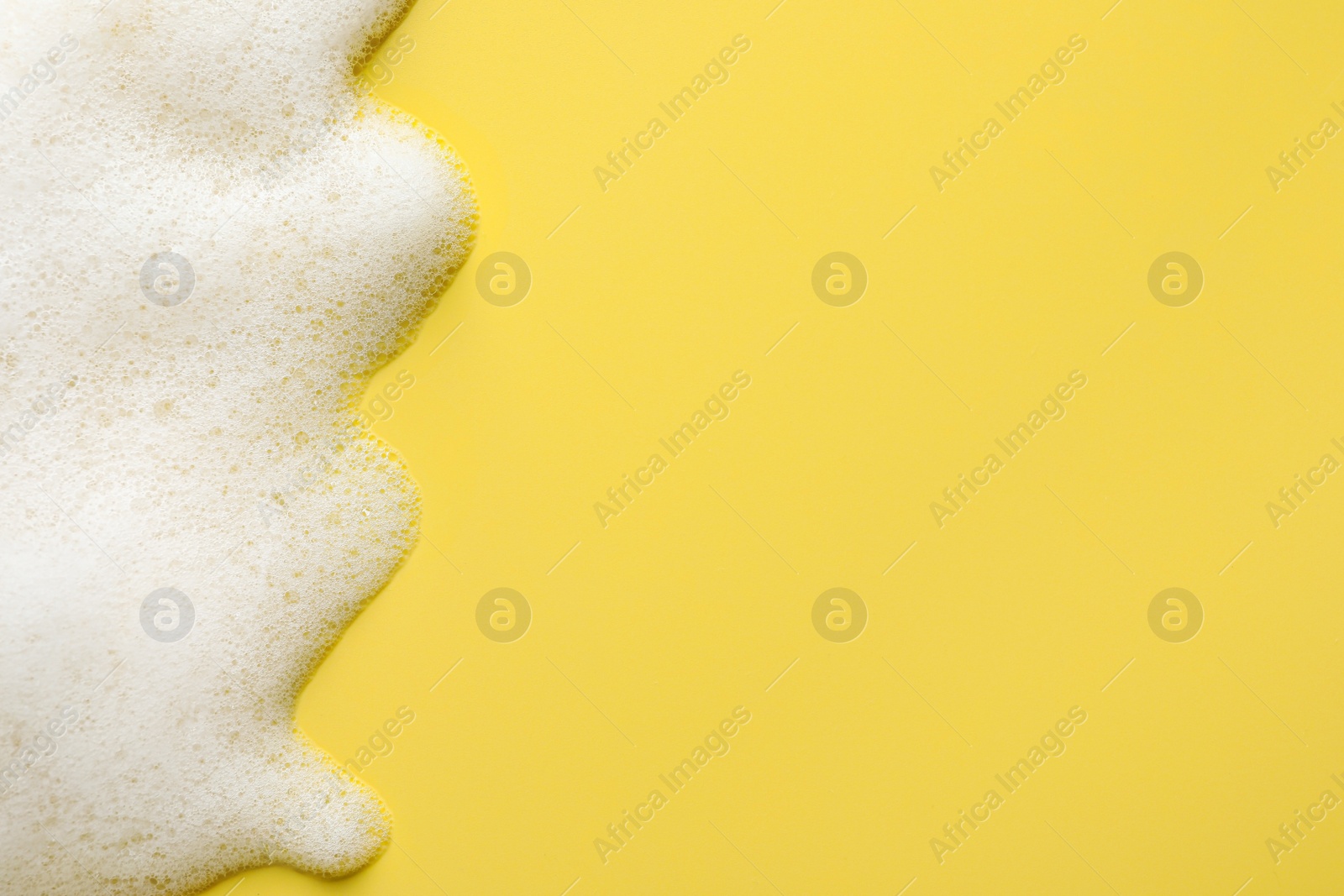 Photo of Fluffy soap foam on yellow background, top view. Space for text