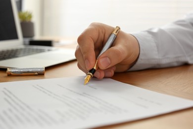 Photo of Notary signing document at wooden table indoors, closeup