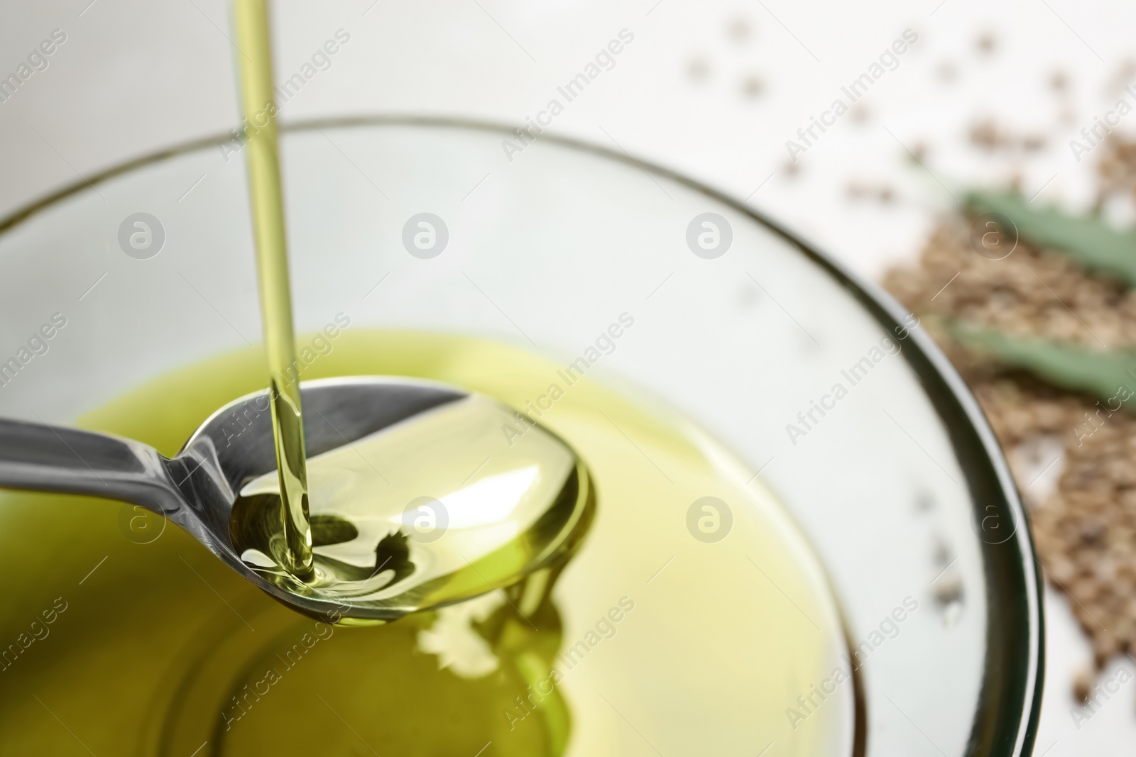 Photo of Pouring hemp oil into spoon over glass bowl, closeup