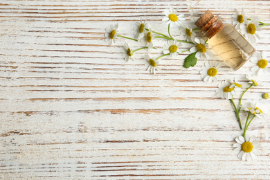 Photo of Bottle of essential oil and chamomiles on white wooden table, flat lay. Space for text