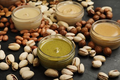 Different types of delicious nut butters and ingredients on black table