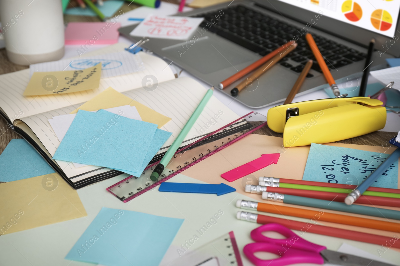 Photo of Laptop, notes and office stationery in mess on desk. Overwhelmed with work