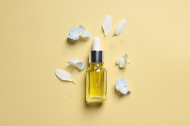 Photo of Bottle of cosmetic serum and beautiful flowers on pale yellow background, flat lay
