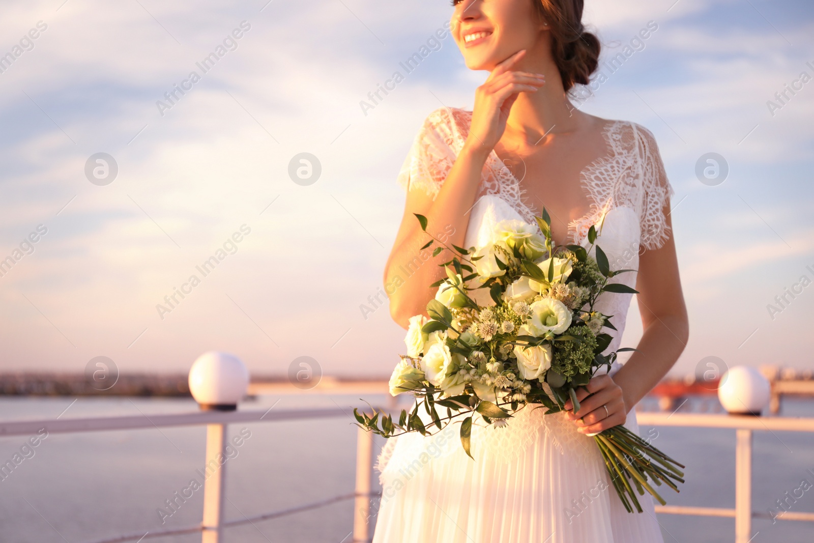 Photo of Gorgeous bride in beautiful wedding dress with bouquet near river, closeup