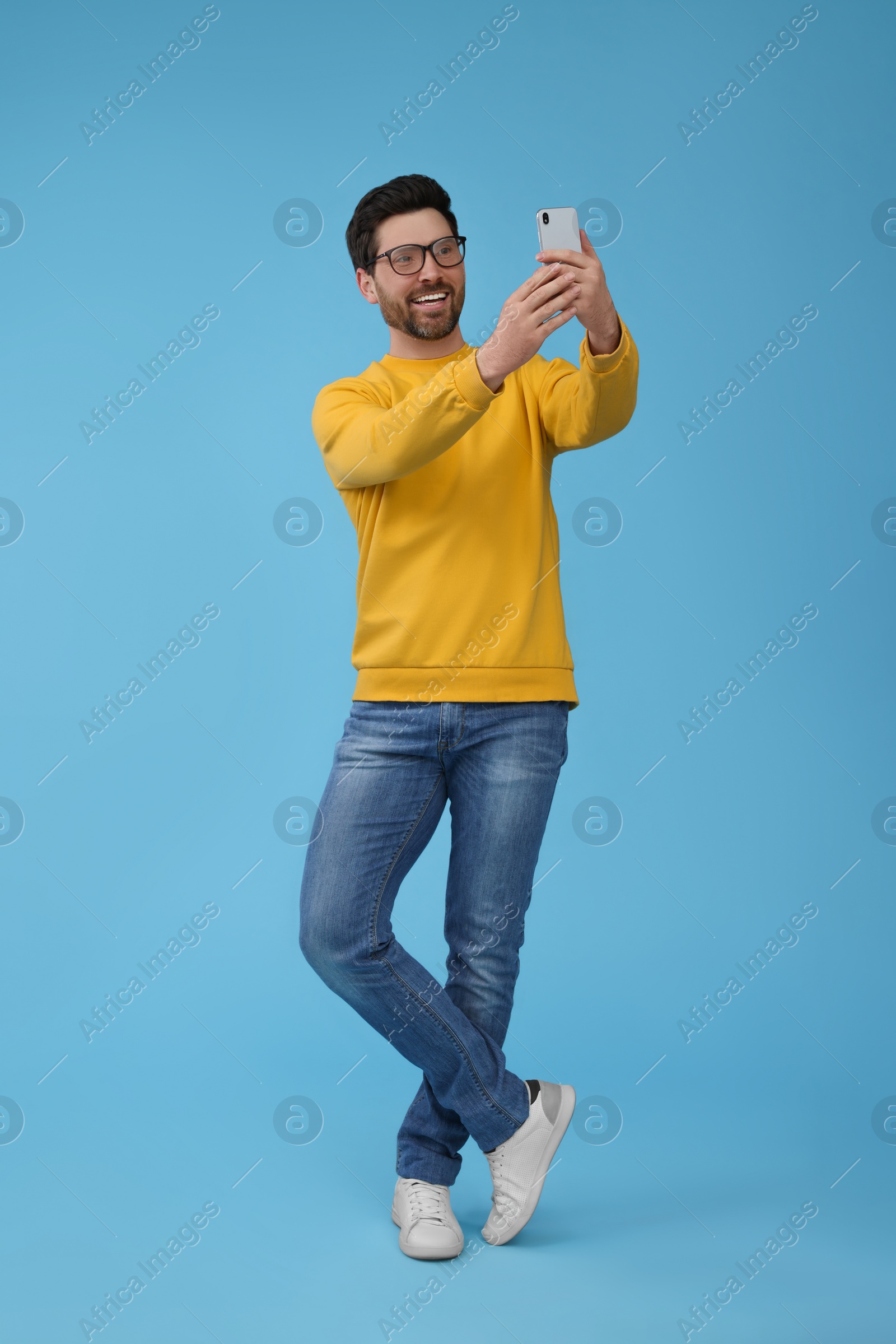 Photo of Smiling man taking selfie with smartphone on light blue background