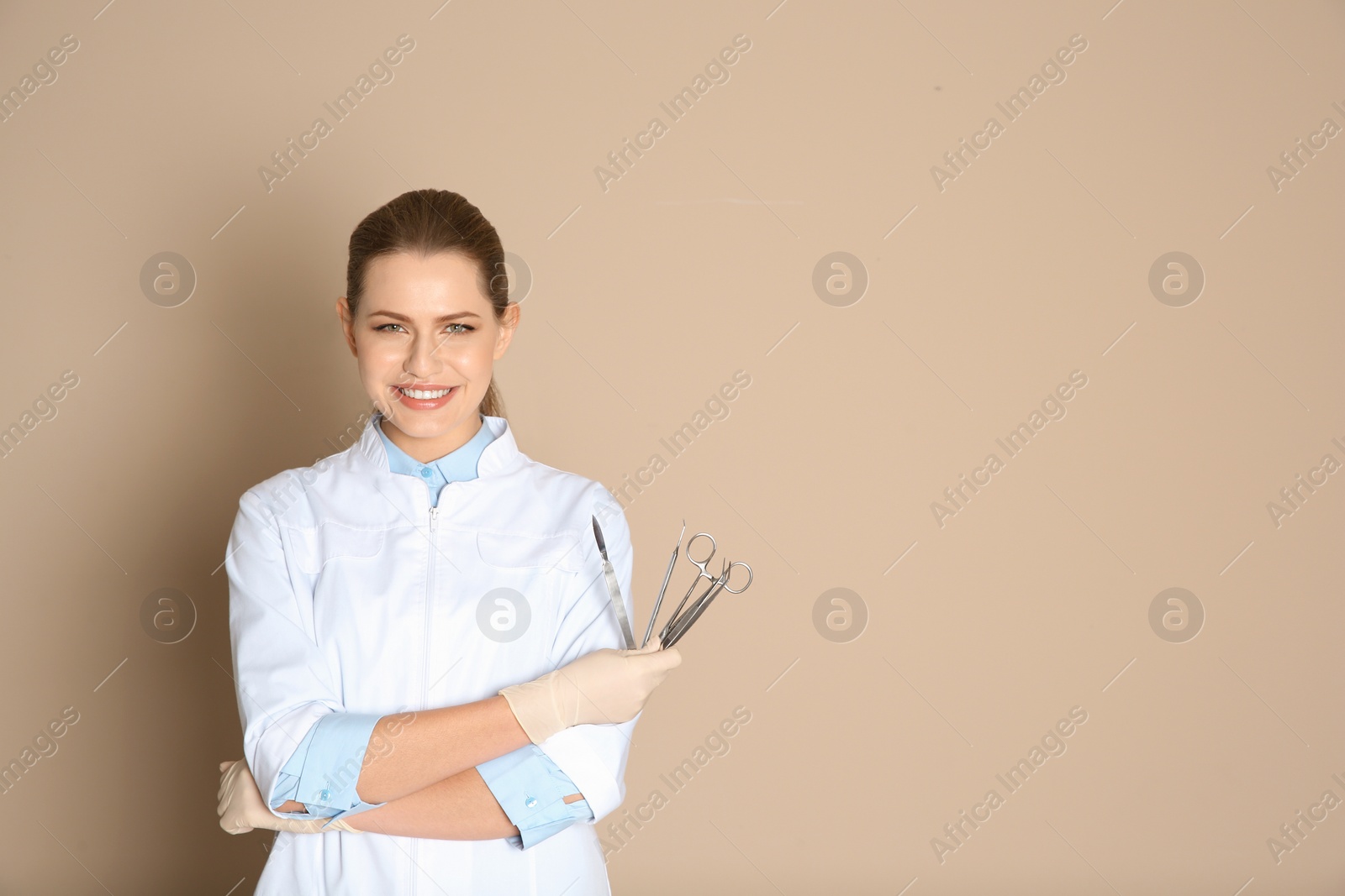 Photo of Female dentist holding professional tools on color background. Space for text